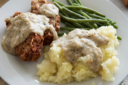 Mashed potatoes covered in gravy with vegan lentil loaf and green beans close up.