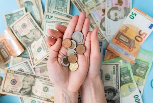 The girl holds coins in her hands against the background of scattered banknotes. International banknotes - dollars, euros, coins. The concept of currency transactions, loans, exchange, gambling