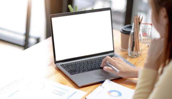 Mockup image of a woman using and typing on laptop computer with blank white desktop screen on wooden table.