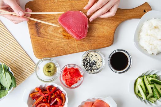 The process of preparing sushi, preparing all the ingredients for sushi, the girl is holding tuna with chopsticks