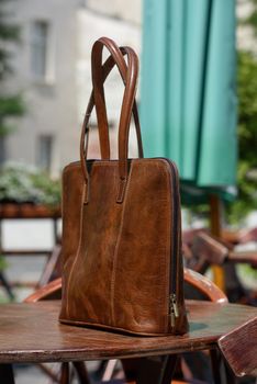 close-up photo of brown leather bag on a wooden table. outdoors photo