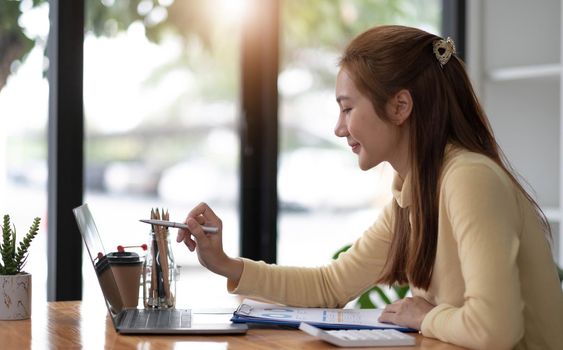 Business woman pen pointing turnover with graph chart report on laptop computer for analysis data.