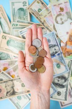 The girl holds coins in her hands against the background of scattered banknotes. International banknotes - dollars, euros, coins. The concept of currency transactions, loans, exchange, gambling