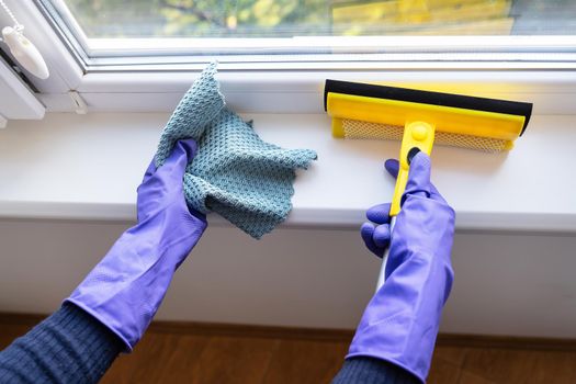 Cleaning and cleaning concept. A young girl in purple gloves holds a rag and a mop for cleaning windows