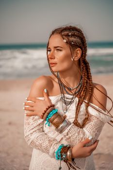 Model in boho style in a white long dress and silver jewelry on the beach. Her hair is braided, and there are many bracelets on her arms