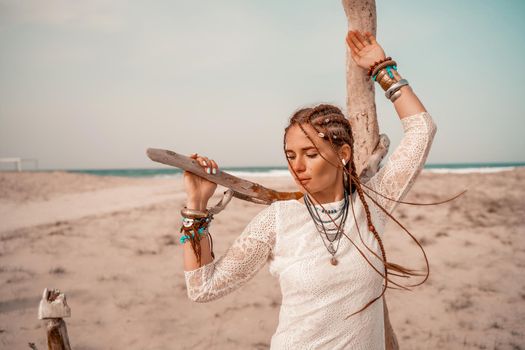 Model in boho style in a white long dress and silver jewelry on the beach. Her hair is braided, and there are many bracelets on her arms