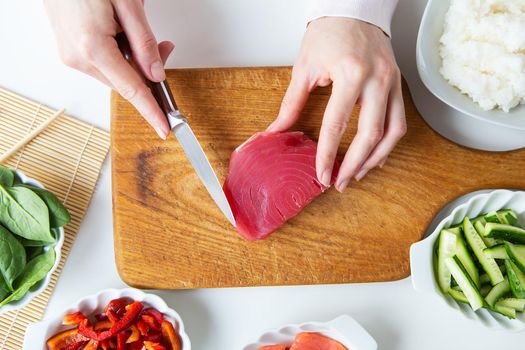 In the process of making sushi, preparing all the ingredients for sushi, the girl cuts the tuna. View from above