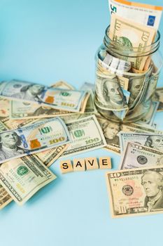 Money in international currency, including the euro, the dollar lies on a blue background next to a jar with banknotes and the inscription save