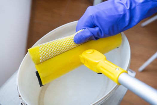 House cleaning and cleaning concept. A young girl in purple gloves squeezes water out of a mop