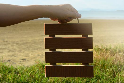 Hands holding wooden frame with blurred background of green grass and ocean. Copy space. Flat Lay.