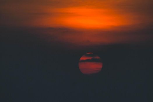 Beautiful sunset. Dramatic Fiery Sun Surrounded by Clouds During Sunset.  Vibrant orange red clouds are back lit by the sun.