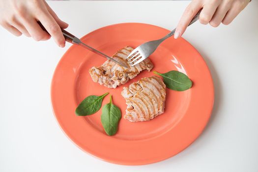 Close-up shot of a juicy delicious grilled tuna steak on a bright coral plate. Delicious and healthy and wholesome food, proper nutrition. The girl is holding a fork and knife