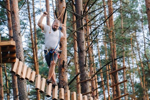 A man overcomes an obstacle in a rope town. A man in a forest rope park.