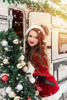 Beauty girl in santa costume decorates the Christmas tree at winter campsite getting ready for the new year. New year celebration concept