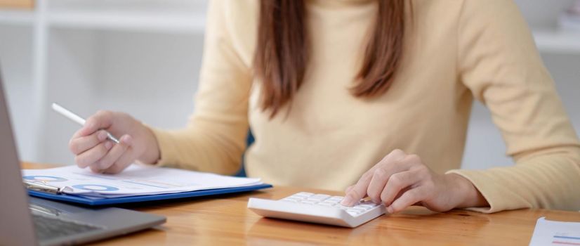 Close up Business woman using calculator and laptop for do math finance on wooden desk in office and business working background, tax, accounting, statistics and analytic research concept.