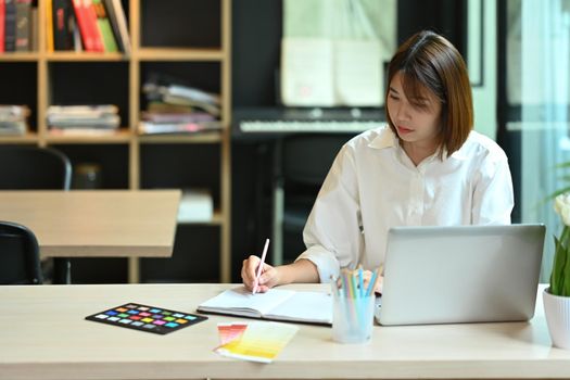 Focused asian woman working on creative project at contemporary workplace.