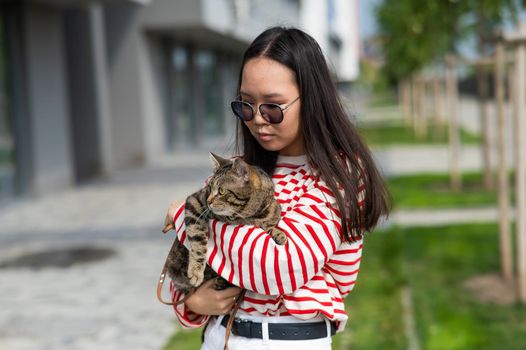 Young woman holding tabby cat in her arms outdoors