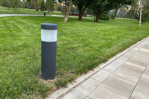 marble path of square tiles, lantern mounted on a green lawn in the park, daylight. copy space.