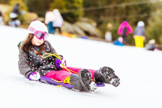 A young girl tobogganing at Lake Mountain on a clear sunny day in Victoria, Australia