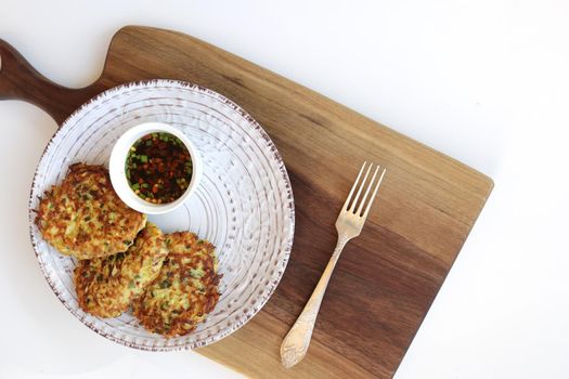 vegetarian zucchini fritters in a white plate and asian sauce with spices in a small white bowl on a wooden cutting board. White background. Vegetarian food concept