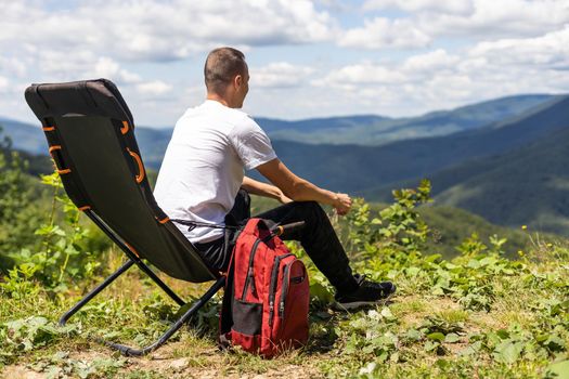 idyllic and rural scene. A man chilling and resting after hiking sitting on a chair and looking in the mountains.