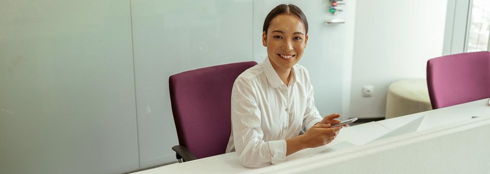 Smiling asian business woman sitting in meeting room and holding phone. High quality photo