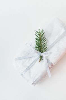 A homemade Christmas stollen sealed in white craft paper, along with a sprig of a Christmas tree, lies on a white background. Gift wrap