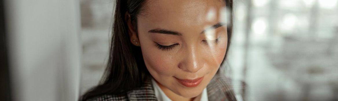 Portrait of smiling asian business woman standing behind glass in office and looking down. Close up