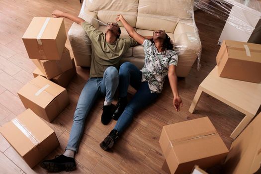 Married couple taking break after moving in together, enjoying new beginnings in apartment flat. Sitting on living room floor and talking about future family, dreaming about achievement.