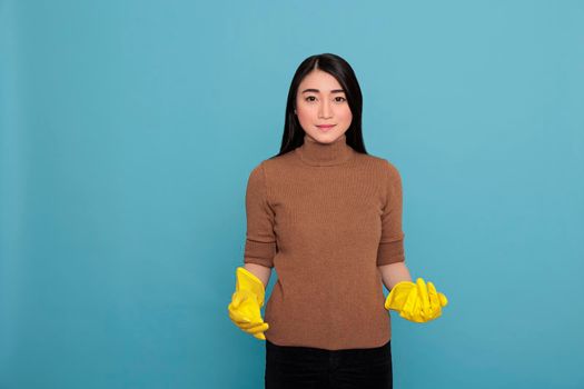 Happy smiling asian housewife from chores wearing yellow gloves standing against a blue background, Cleaning home concept, Cheerful satisfied and glad with positive state of mind
