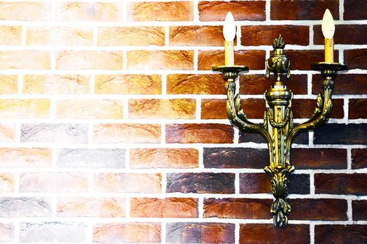 Bronze golden candlestick on a bright red brick wall with light space for text. a support or holder for one or more candles, typically one that is tall and thin.