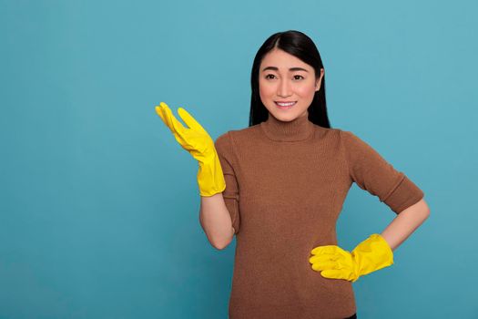 Happy glad and smiling asian woman gesture with her hand wearing yellow rubber gloves gesture with her hand, Cleaning home concept, Satisfied cheerful and laughing nursemaid