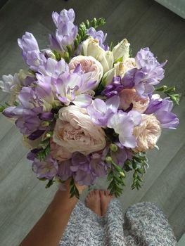 Top view of the hands of a young female florist creating a beautiful composition of delicate pink roses, carnations and white daisies. Business flower shop. Making a bouquet.