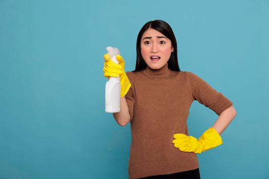 Shocked surprised asian housekeeper from chores holding spray in yellow glove ready for duty, Cleaning home concept, Amazed wondering woman and negative from day to day work