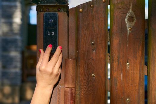 a bell in a building which can be rung by visitors outside to signal their arrival. Woman's hand pressing a doorbell on a wooden fence in the garden.