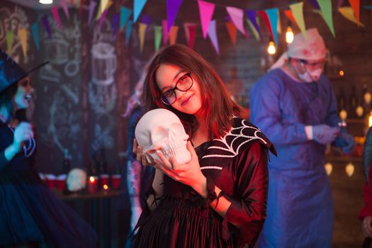Portrait of young witch showing affection to her human skull at a halloween celebration. Young and creepy girl.