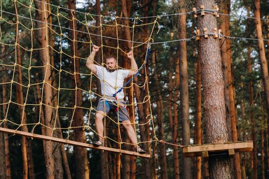 A man overcomes an obstacle in a rope town. A man in a forest rope park.