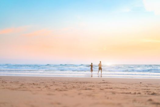 Couple running on the beach. Happy couple go to swim in ocean at sunset. Blurred summer vacation background. Defocused man and woman run on sandy sea beach. Summertime. Happy people
