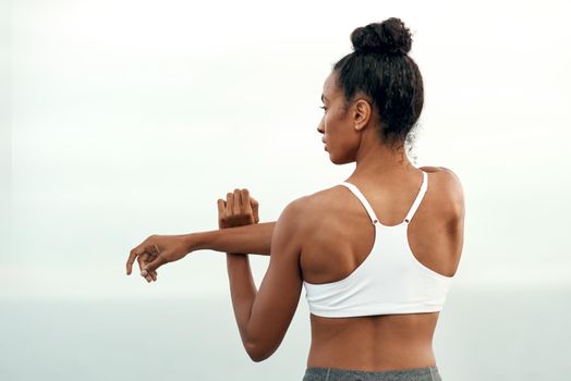 Change will come through every movement. Rearview shot of a sporty young woman stretching her arms while exercising outdoors