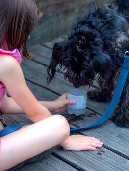 girl waterng her dog outdoors with a plastic recycled water bottle