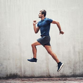Skip over every hurdle until you reach your goal. a sporty young man running against a grey wall outdoors