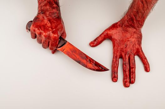 A man with bloody hands holds a knife on a white background