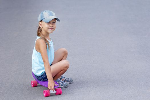 Caucasian smiling child sitting on skateboard on road in summertime