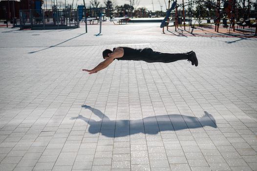 A man in black sportswear jumps doing push-ups in the park