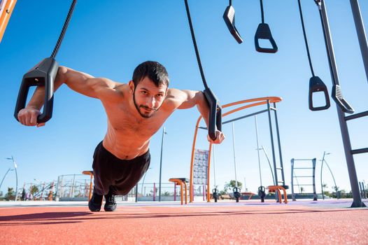 Shirtless man doing loop exercises outdoors