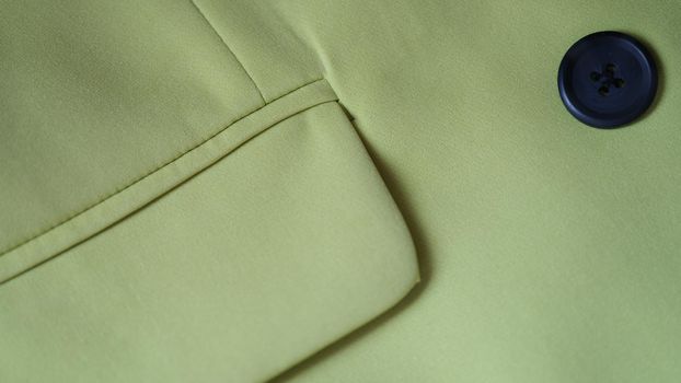 Closeup of green jacket with black button and pocket. Details of stylish green jacket