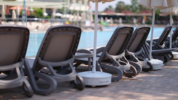 Beautiful sun loungers by pool in nature against backdrop of hotel. Summer vacation relax and hotel service for tourists