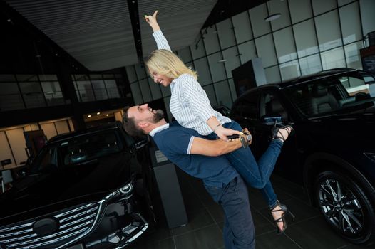 Happy caucasian couple hugging while buying a new car in a car dealership