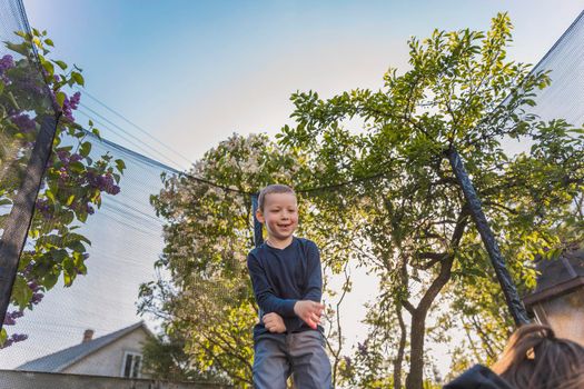 little boy jumps on a trampoline that stands in the yard