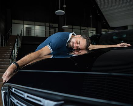 Happy caucasian man hugging the hood of his new car in a car dealership